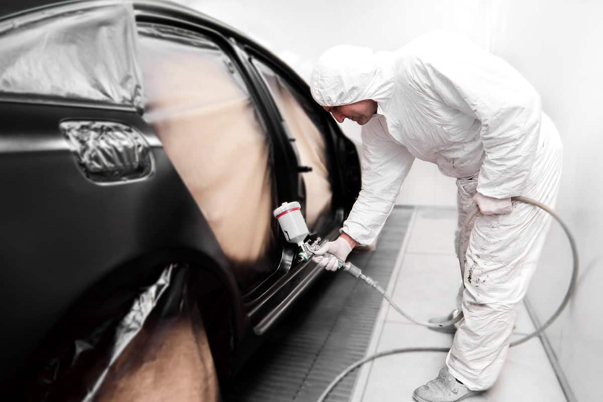 Mechanic painting a black car in workshop