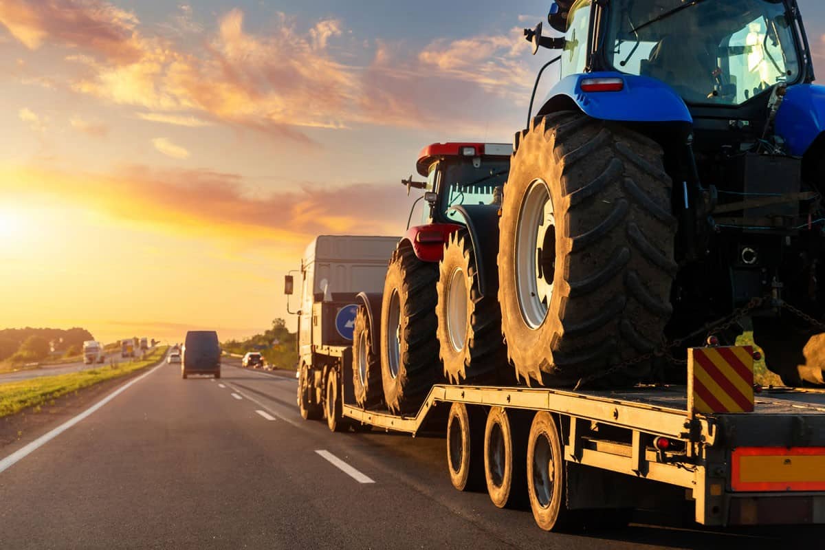 POV heavy industrial truck semi trailer flatbed platform transport two big modern farming tractor machine on common highway road at