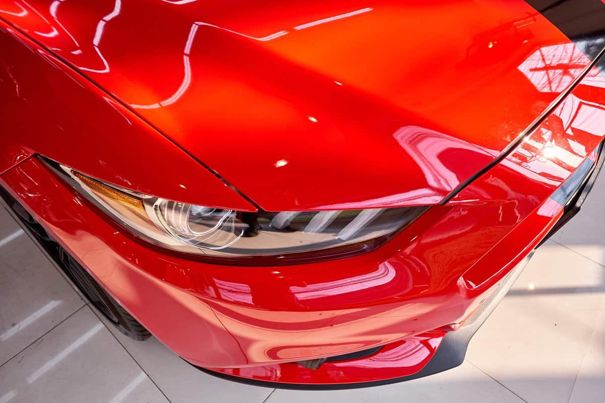 Shiny red Ford Mustang bonnet & headlight with reflection on hood. Luxury sportscar after ceramic coat. Car detailing & automotive background. American muscle