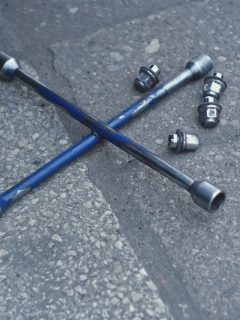 Shiny Metal Security Lug Nuts for Car Wheel Hub Mounting Screws and Cross Wrench Laying on Ground Outside of Mechanic Workshop - Can I Reuse Axle Nut