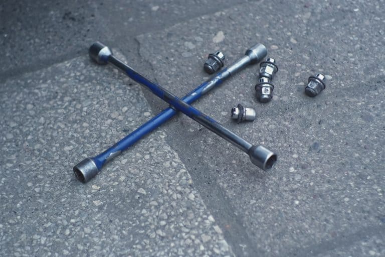 Shiny Metal Security Lug Nuts for Car Wheel Hub Mounting Screws and Cross Wrench Laying on Ground Outside of Mechanic Workshop - Can I Reuse Axle Nut