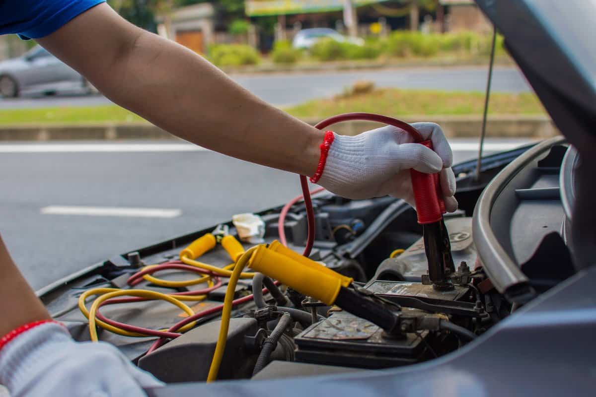 The technician uses a booster cable to connect the dead battery. Electric vehicle battery charging via jumper cable