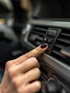 Woman adjusting interior temperature while driving on the road, Female driver is adjusting the air conditioner of the car - Car AC Does Not Turn On Right Away - Why What To Do