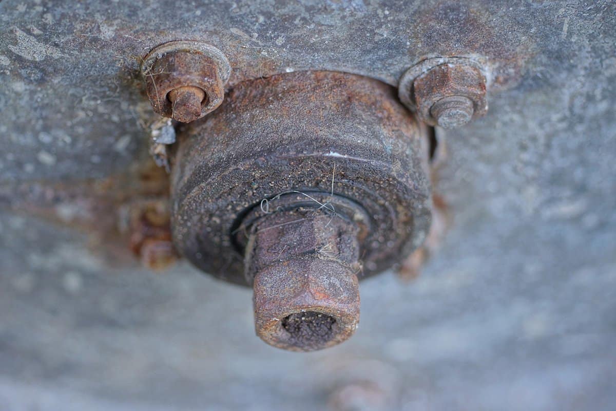 brown rusty iron bolts and nuts with an axle on a gray metal panel