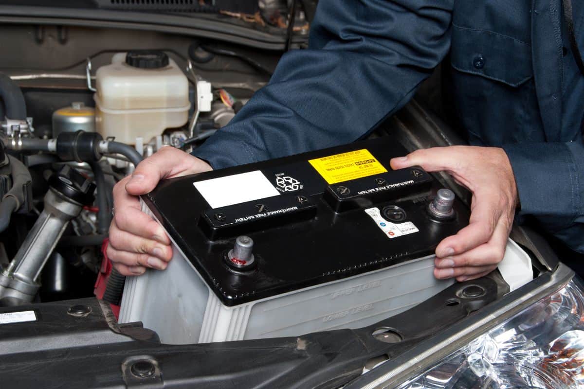 A car mechanic replaces a battery during maintenance.