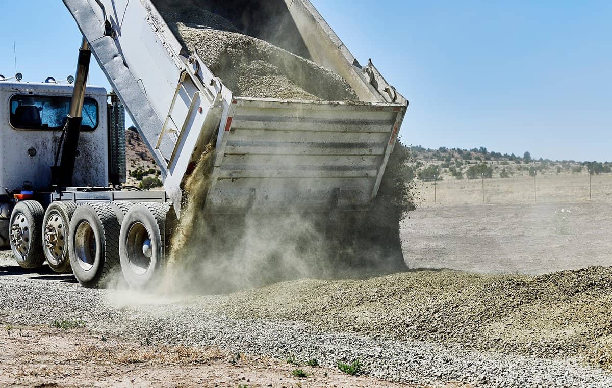 A dump truck spreading gravel on a dirt driveway
