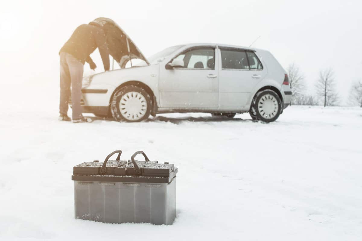 A man repairs a car in winter on snow in the background is a discharged battery