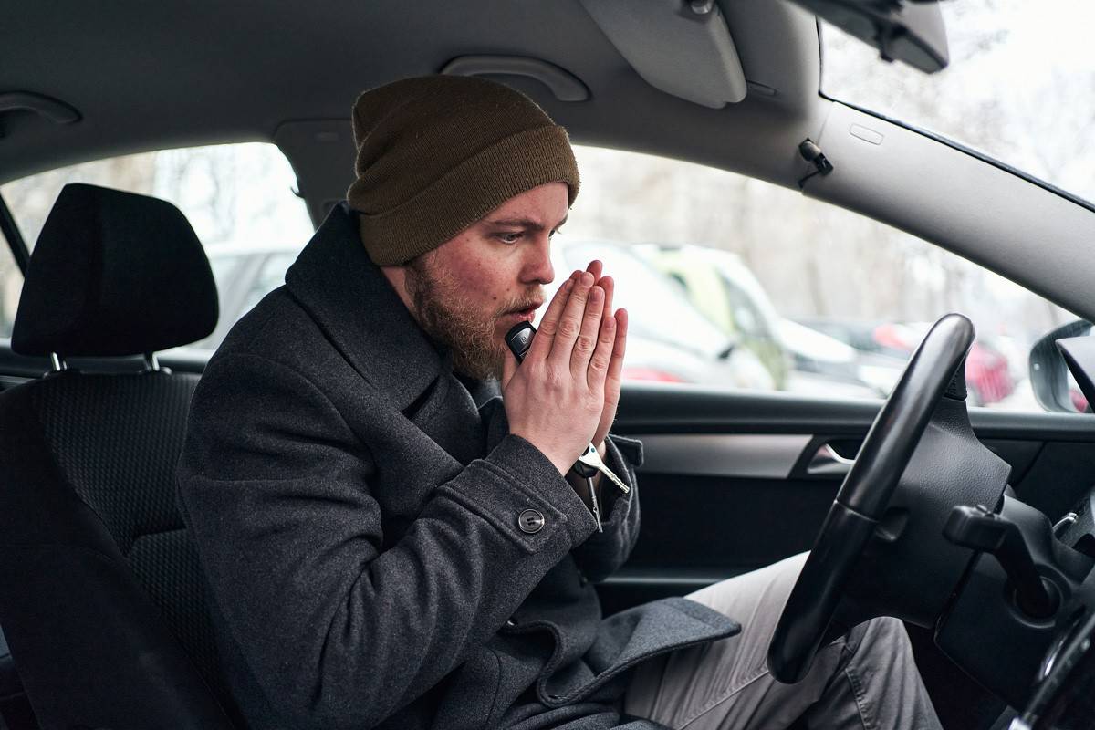A modern young man in his car rubbing and blowing hi hand so he can warm up himself.