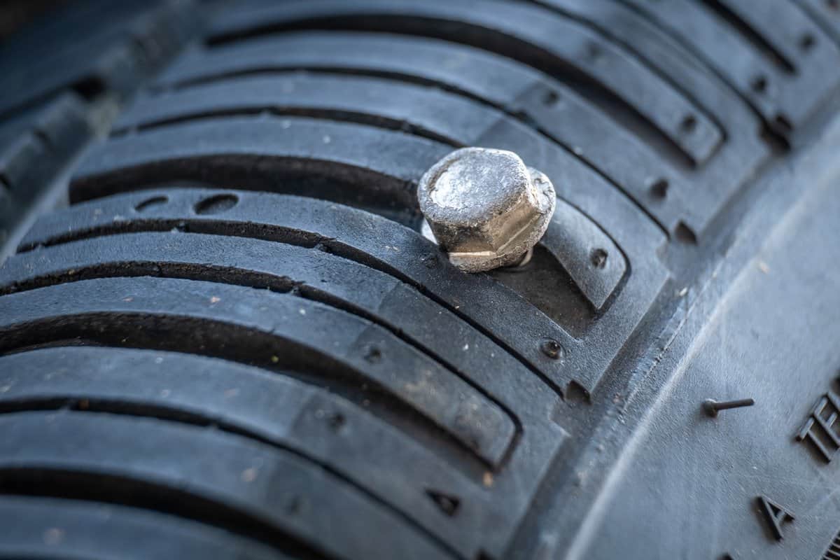 A screw has punctured a car tire at the edge of the tread near the sidewall, rendering the tire irrepairable. 
