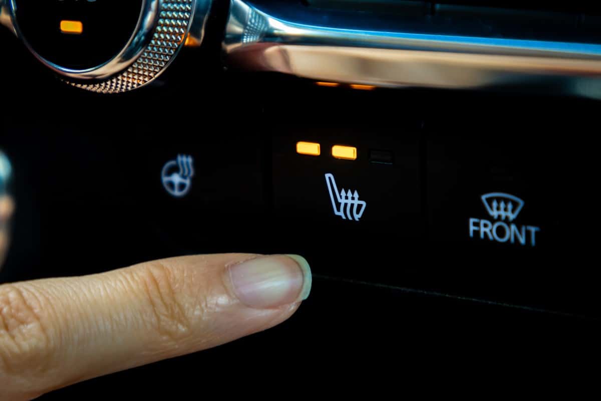 A woman presses a seat heating button inside a car in the winter.