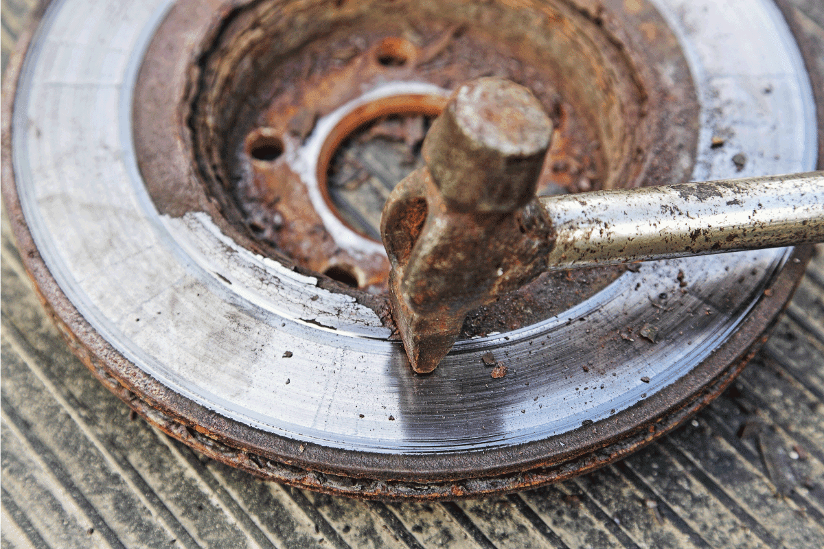 Beating off rust with a hammer from an old rusty brake rotor disc