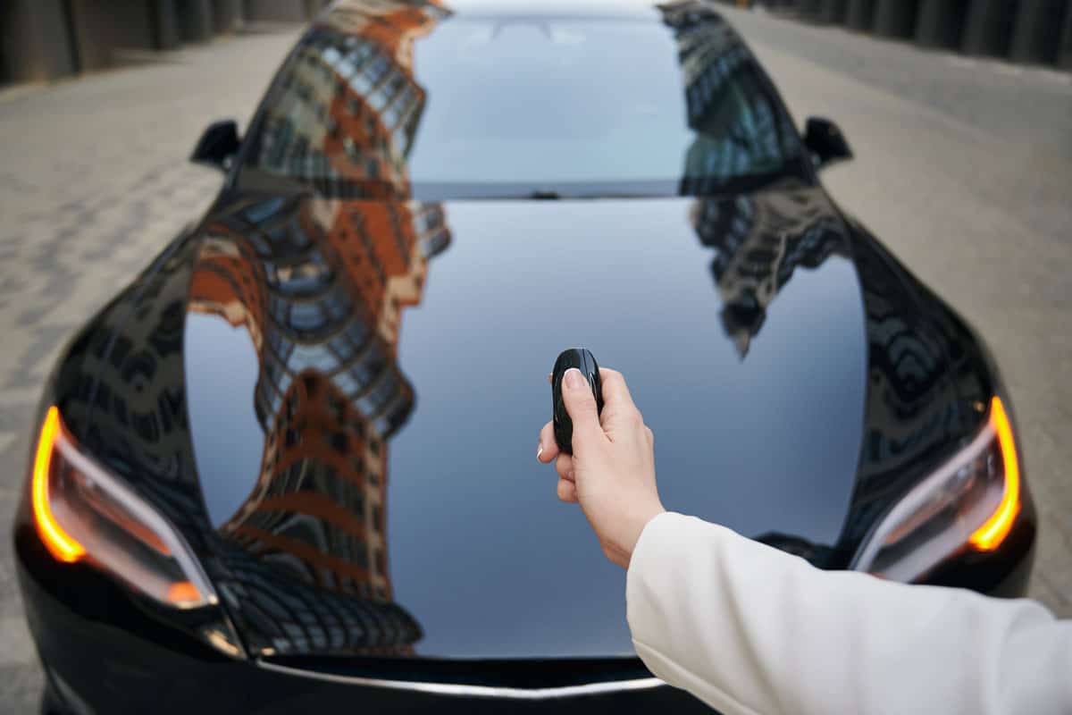 Female arm holding car key on the background of luxure modern black auto