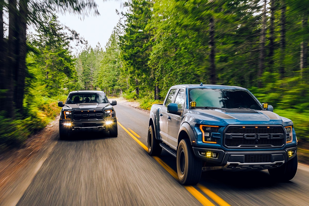 Ford Raptors driving on a two-lane road in the forest