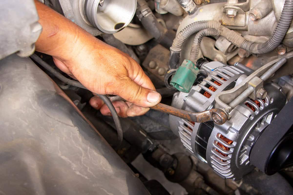 Mechanic or worker hand-holding wrench repair car alternator in a garage. Repairing and maintenance automobile concept. 