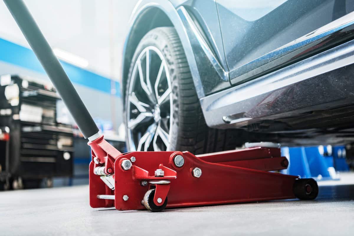 Modern Vehicle and the Floor Jack Lift Vehicle Servicing and Maintenance Inside Auto Service Center.