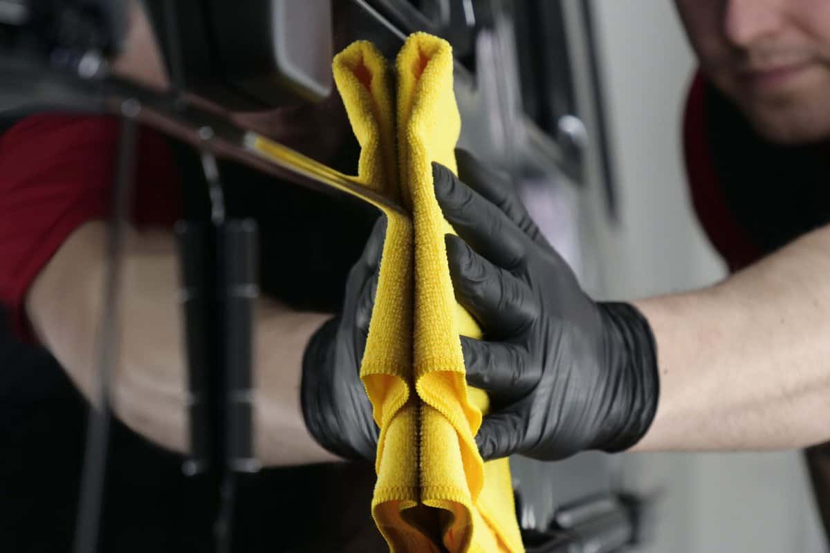 Professional worker guy (Man) wipes the car after painting (ceramics) in a special uniform with black gloves and with a yellow rag. Concept of Young master, Preparing for the sale, Cleaning.
