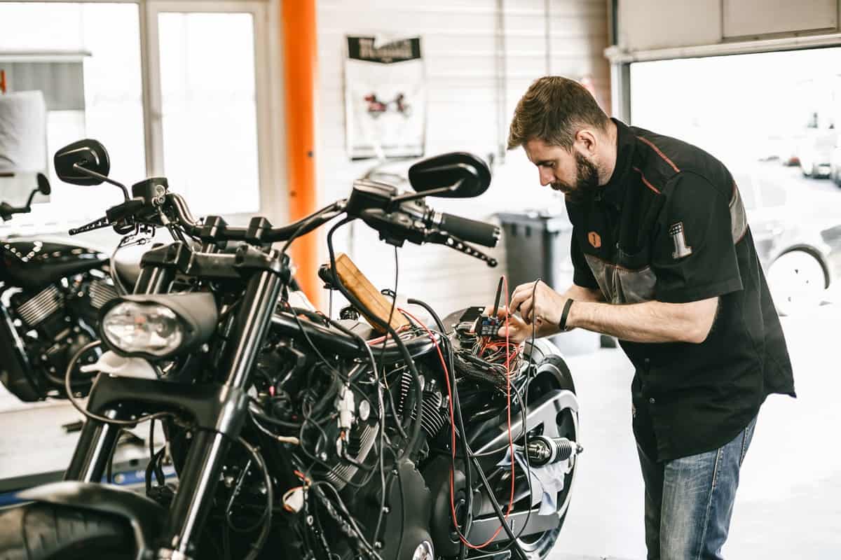 Professional motorcycle mechanic working in bike repair service. Mechanic checking a bike battery level with voltmeter in garage.