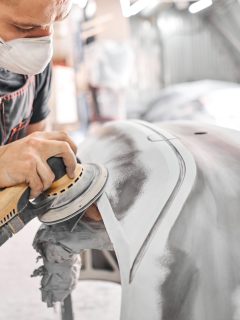 The mechanic works with a grinding tool. Sanding of car elements. Garage painting car service. Repairing car section after the accident - How Many Gallons Of Paint Do I Need To Paint A Car Or Truck [By Size Class]
