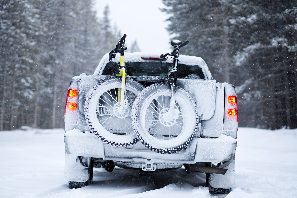 Two fat bikes are transported on the tailgate of a truck during a snowstorm. Fat bikes are mountain bikes with oversized wheels 