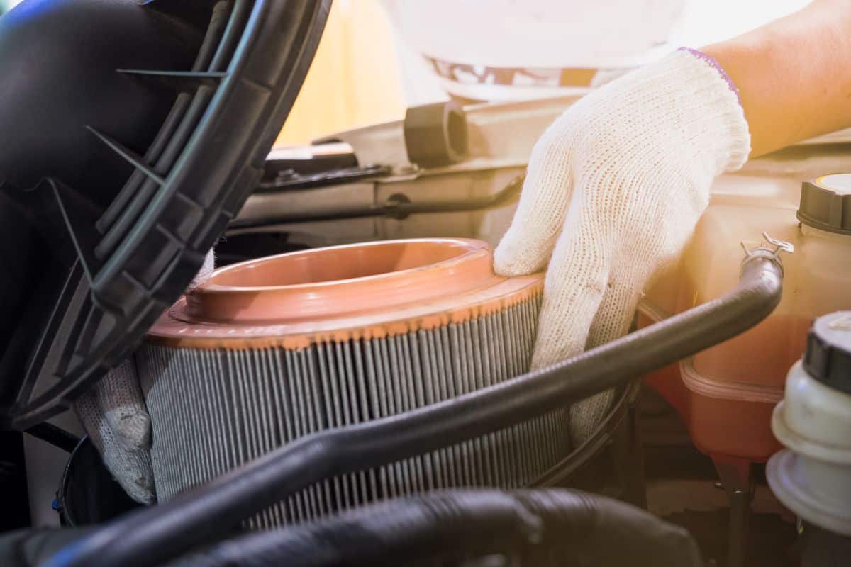 Auto mechanic wearing protective work gloves holding a dirty, air filter over a car engine for cleaning