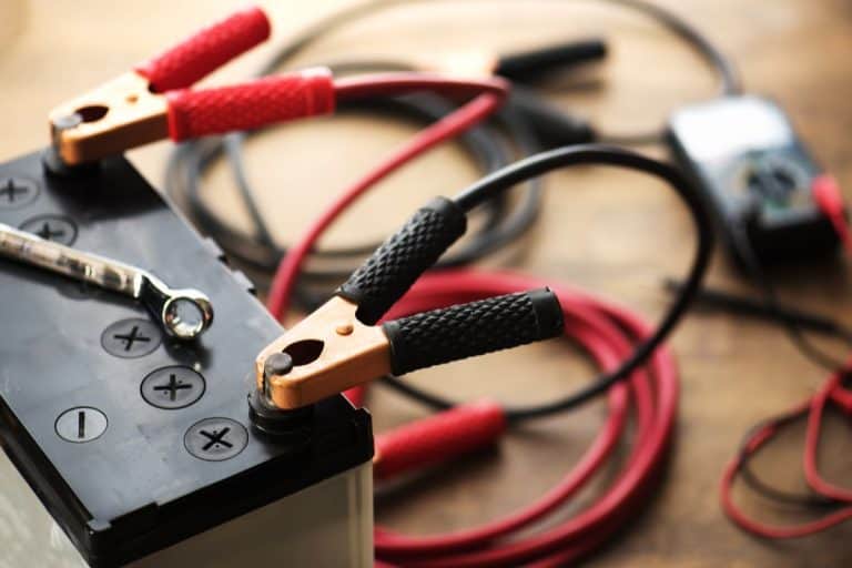 A Car battery with red and black battery Jumper Cables with copper clamps attached to the terminals. - Can You Charge A Car Battery With Two Chargers