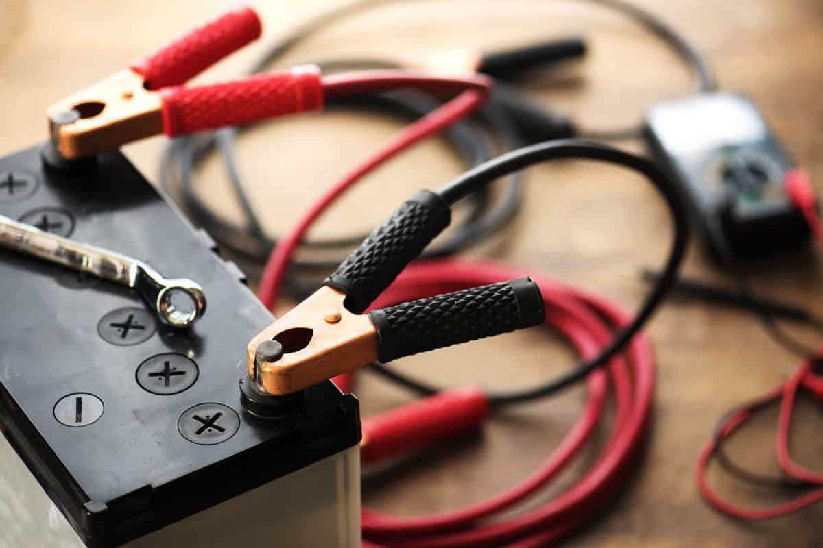 A car battery with red and black battery jumper cables with copper clamps attached to the terminals