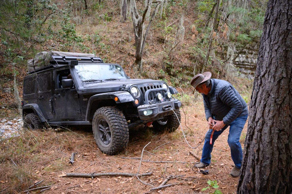  A man is helping to climb an obstacle a jeep with the vehicle winch.