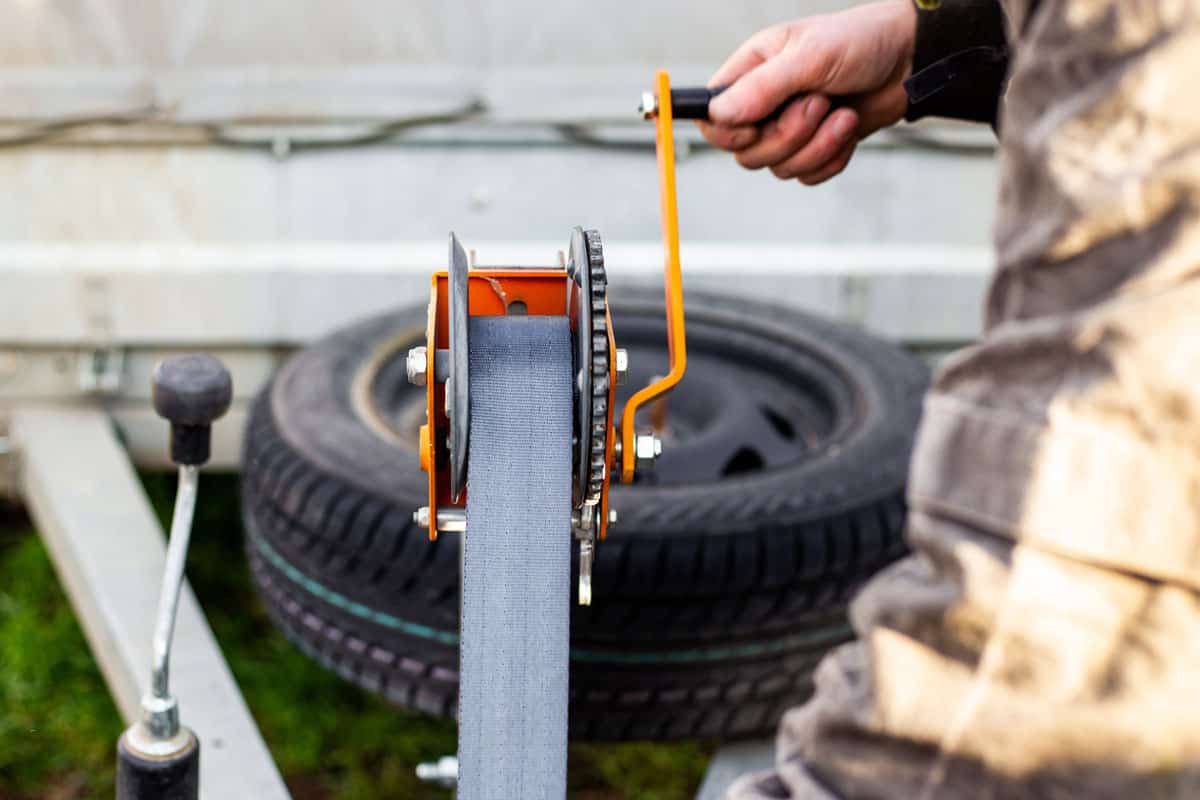 A man spins the winch handle on a car trailer. Towing and transportation of special equipment, loading a