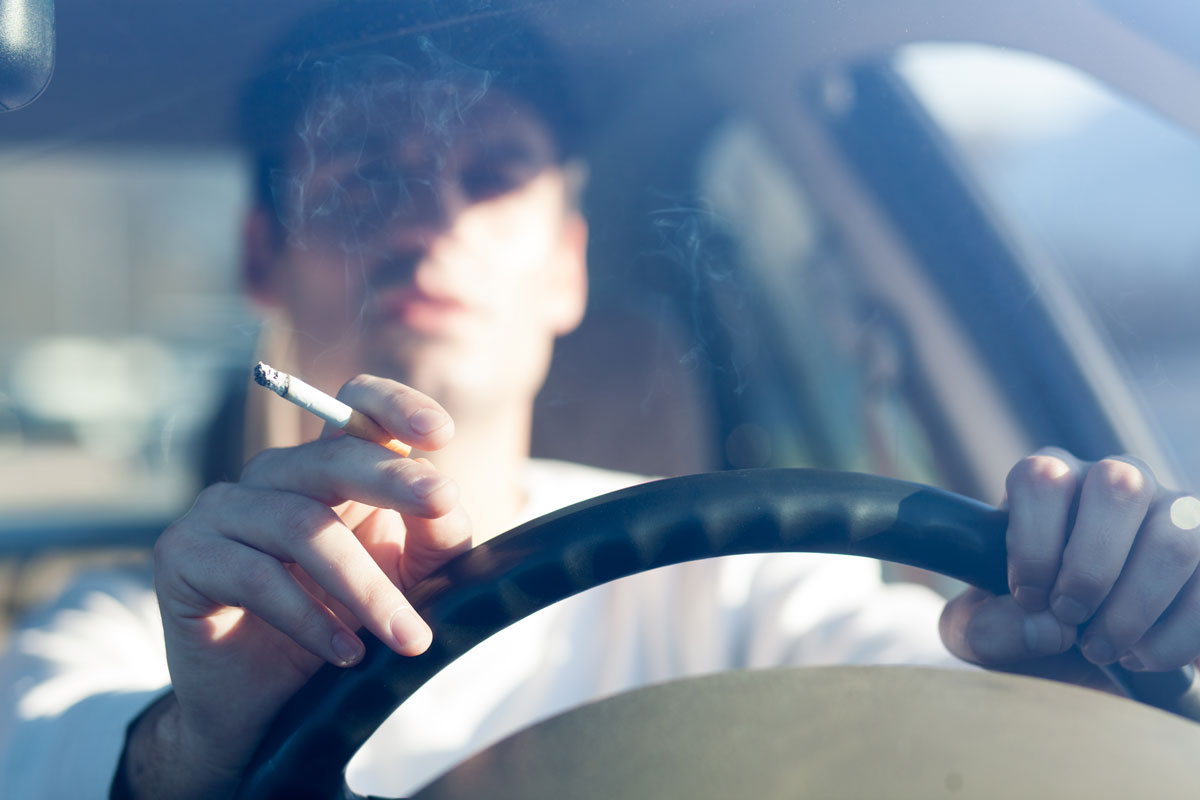 A person in a car driving at the same time smoking