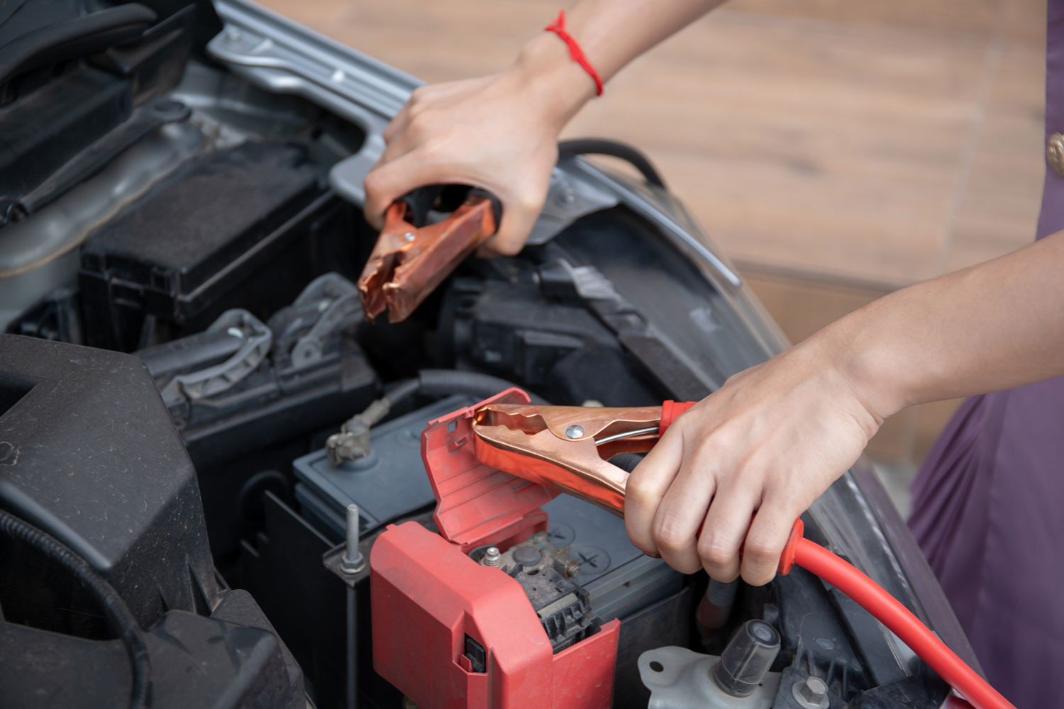 Asian young woman charging a car battery from the other car by using battery connector jump between battery