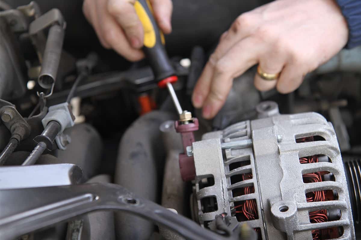 Auto mechanic replacing an alternator in a car