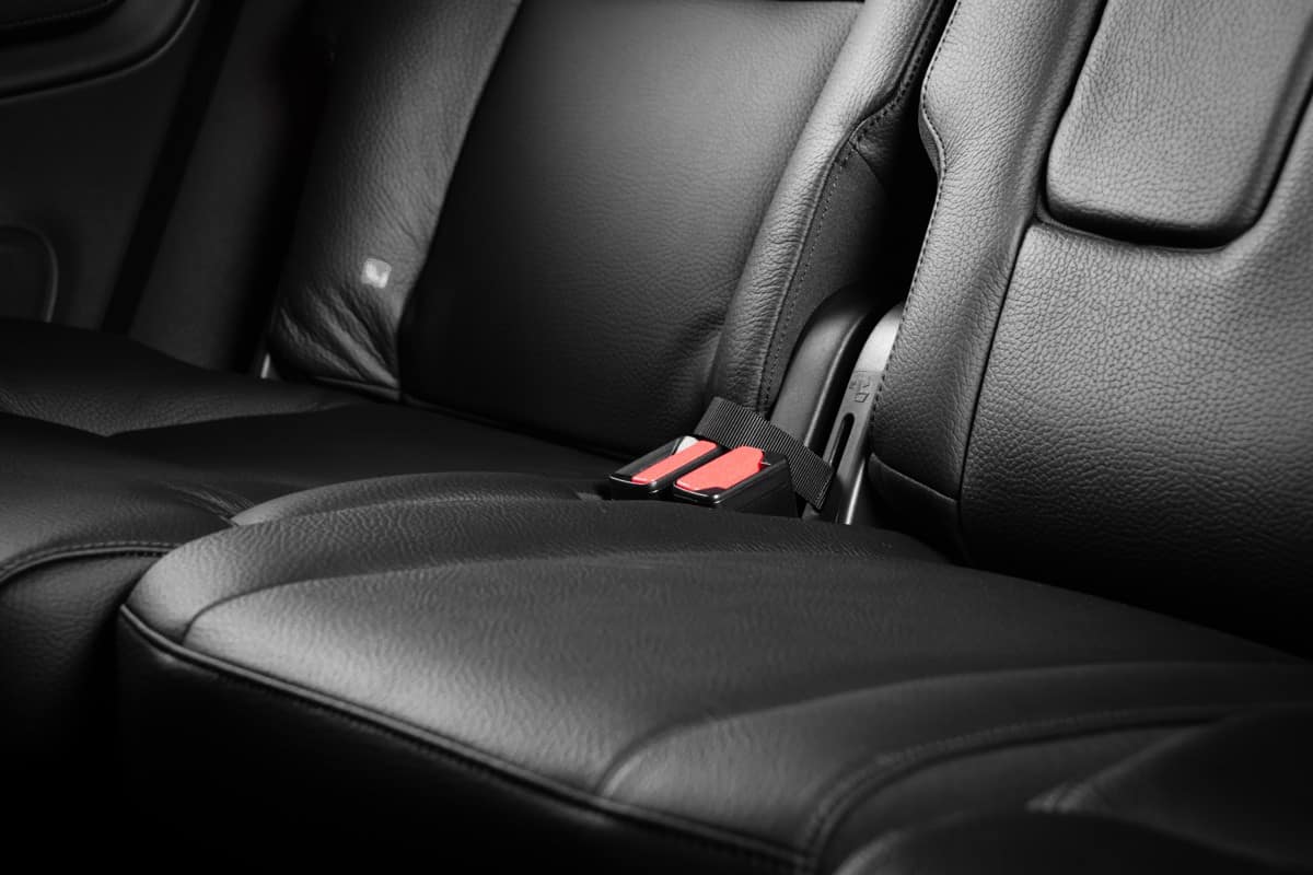 Black leather back seats inside luxury car with red seat belts plugs
