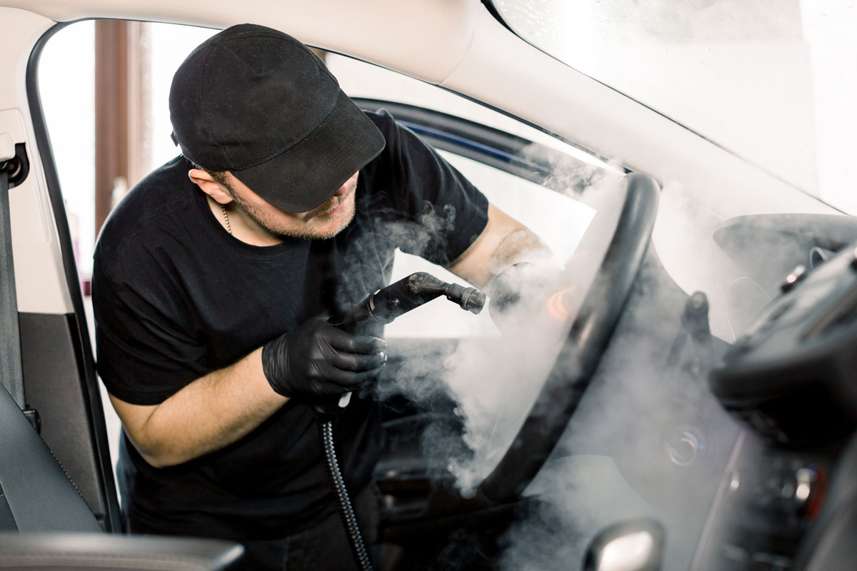 Man in black t-shirt and cap cleaning car interior