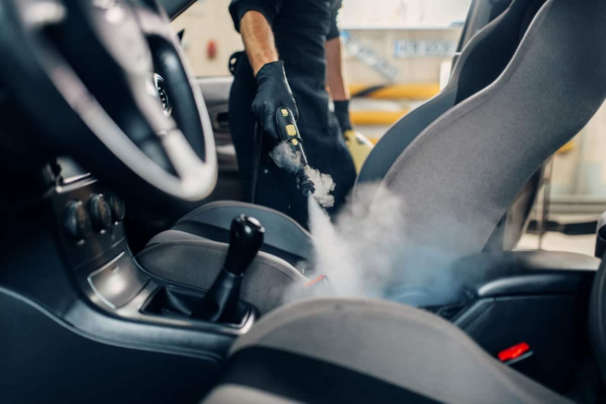 Carwash, worker cleans seats with steam cleaner 