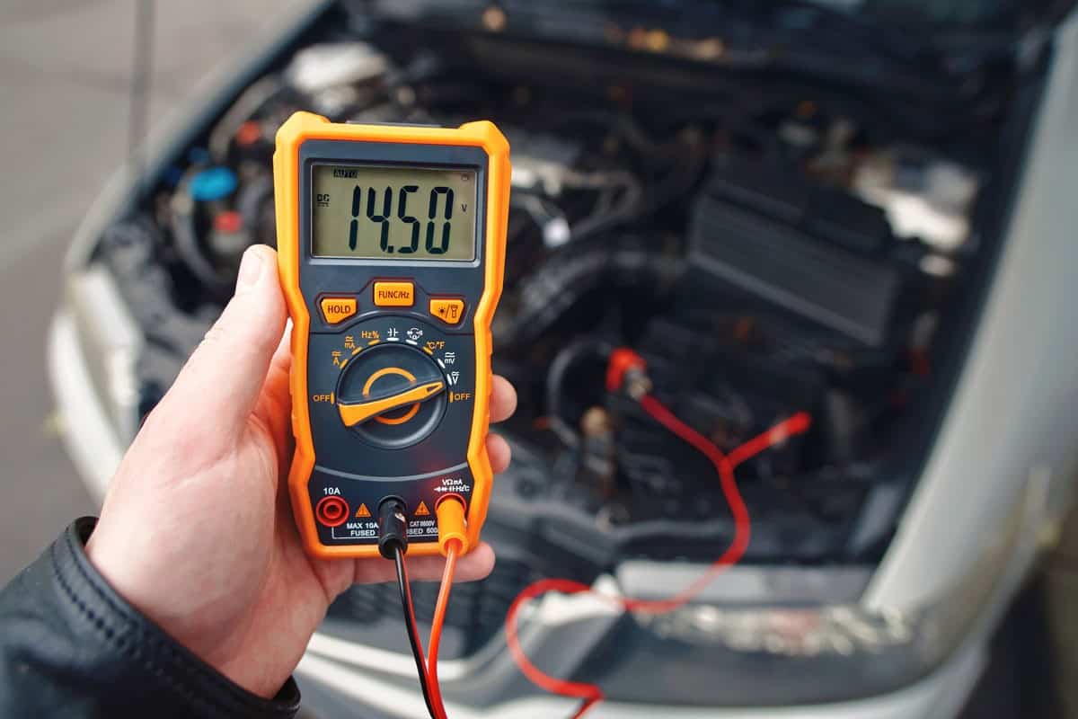Check car battery using voltmeter. Man check up voltage level, alternator produce 14.5 volts with the engine idling
