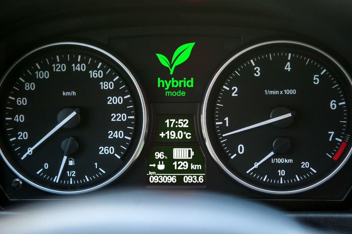 Close up of car dashboard with green hybrid mode icon on. 