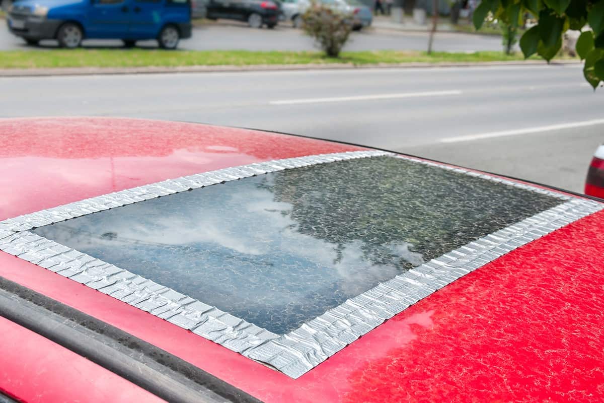 Damaged glass roof window or sunroof on the red car glued with duct tape