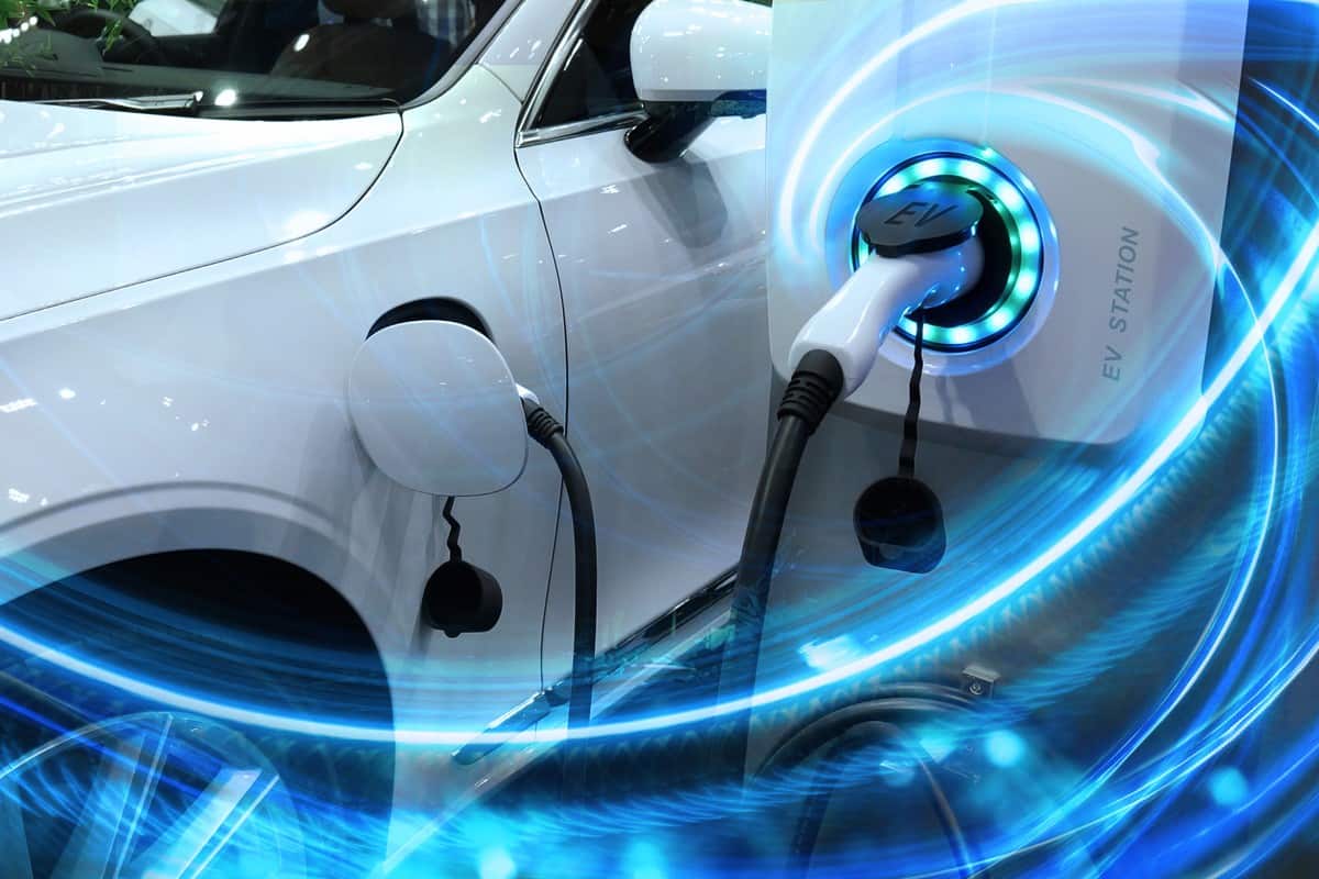 EV Car or Electric vehicle at charging station with the power cable supply plugged in on blurred nature with blue enegy power effect.