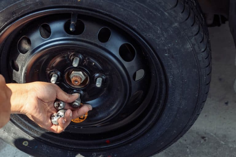 Hands of mechanic pick up the nut of car wheel.Change a flat car tire at car park with Tire maint, What Are Lug Nuts On A Tire & What Do They Do? [With Types And Pictures]