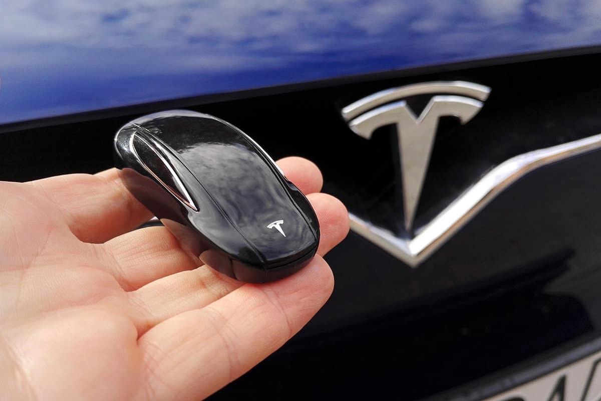 Key for Tesla car on hand with Tesla Model X car front with logo in background
