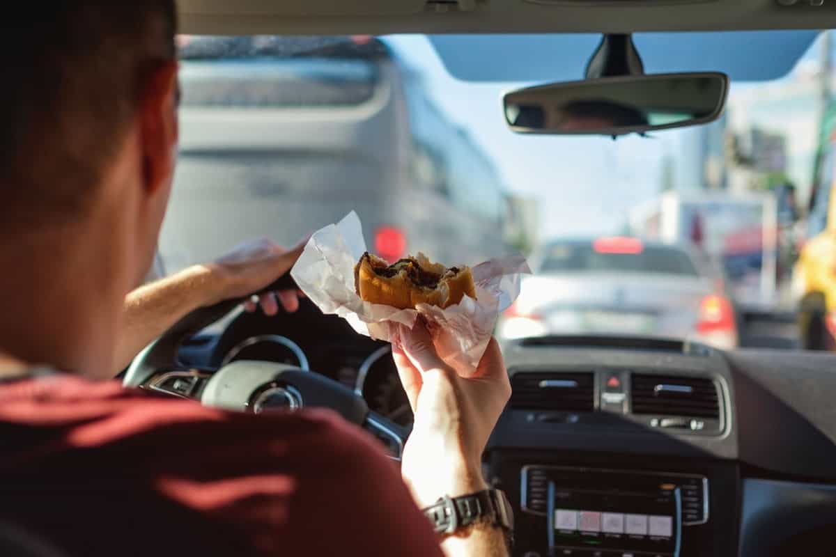 Man driving car while eating hamburger. Waiting and standing in traffic jam 