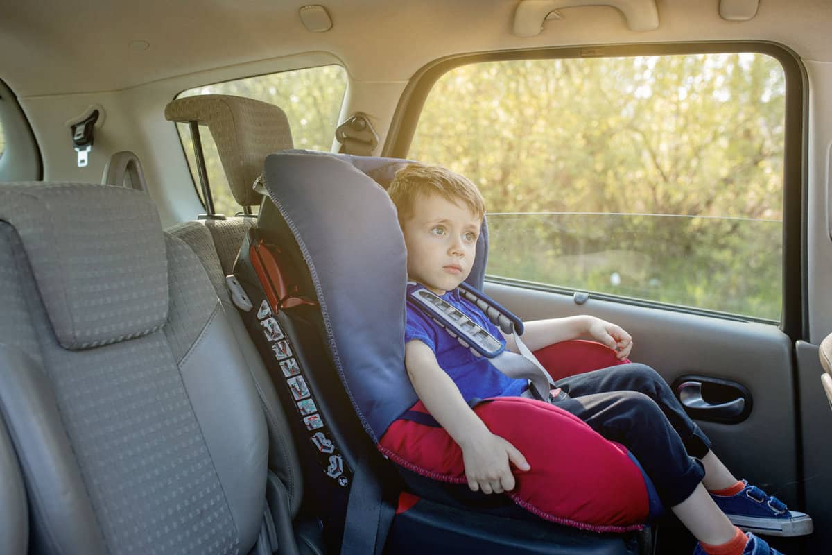 Preschool cute 3-4 years old boy sitting in safety car seat and crying during family travel by car, bad mood, negative emotion, upbringing and family concept, summer outdoor. 