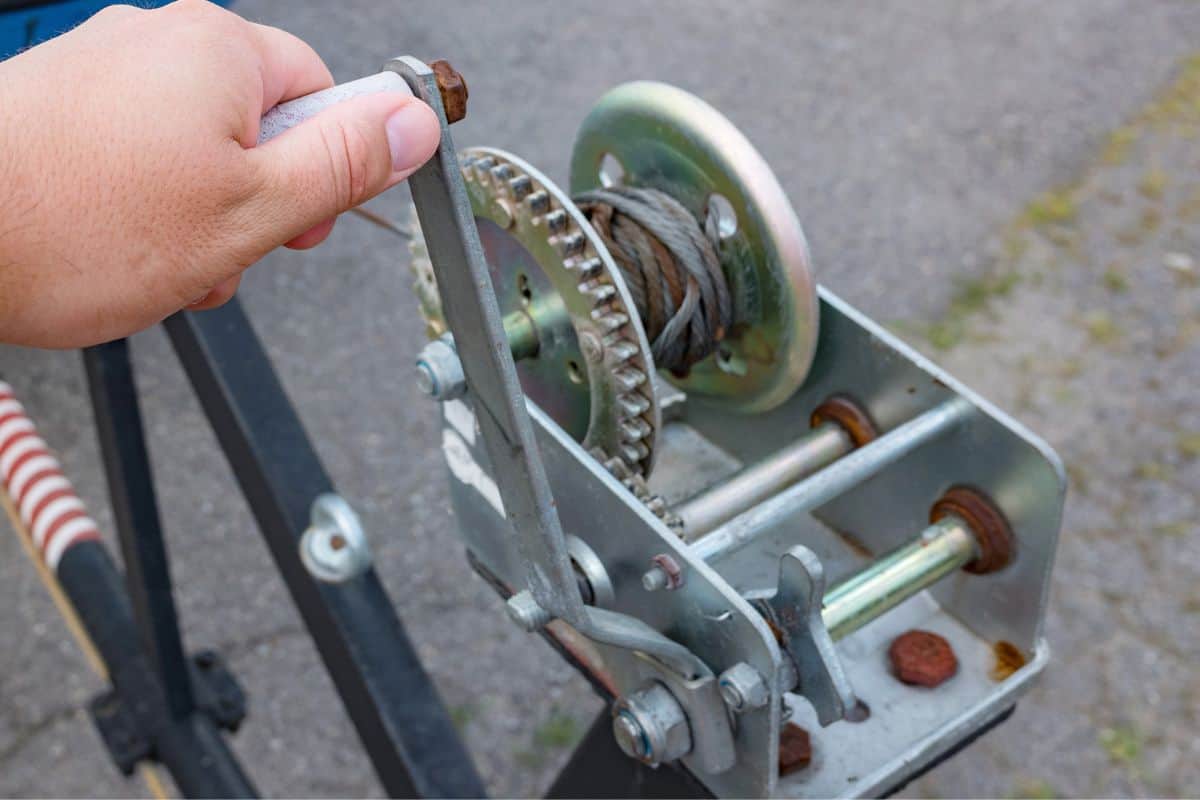 Hand turns the lever handle of the crank boat trailer winch