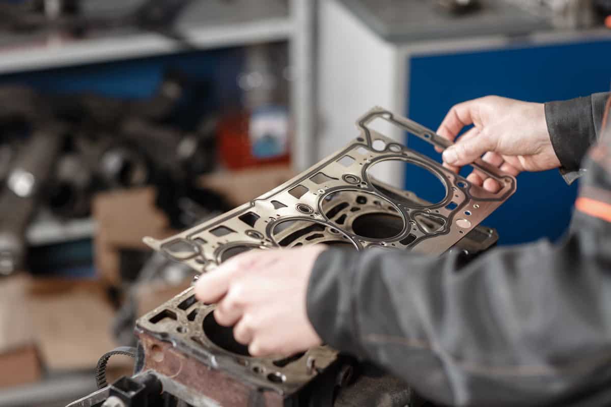 Sealing gasket in hand. The mechanic disassemble block engine vehicle. Engine on a repair stand with piston and connecting rod of automotive technology. Interior of a car repair shop. 