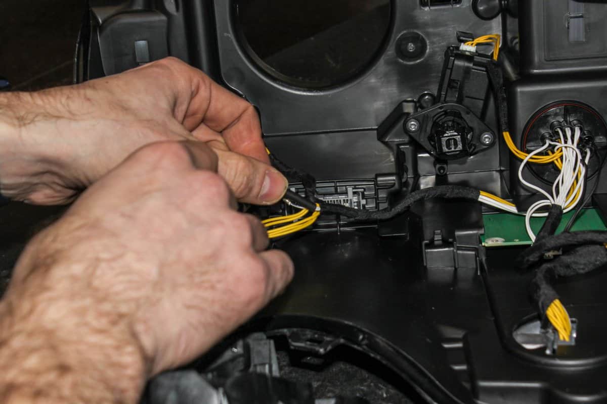 The car headlight is disassembled. Car headlight repair close-up. An auto mechanic repairs the headlight of the car. The master connects the wires in the headlight.