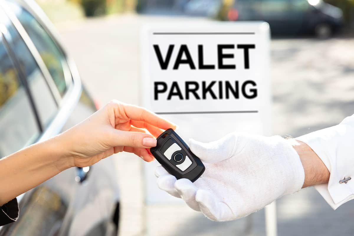 Woman's hand giving car key to male valet near valet parking sign