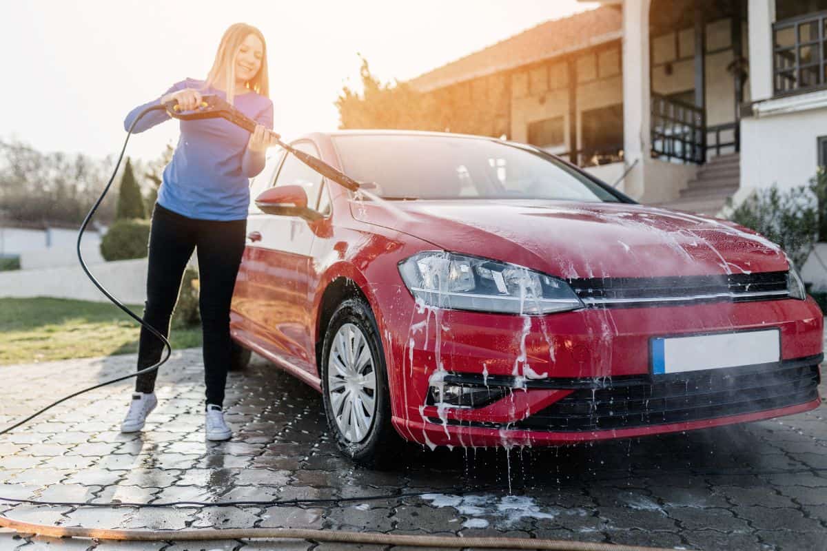 Young woman washing her car using high pressure water
