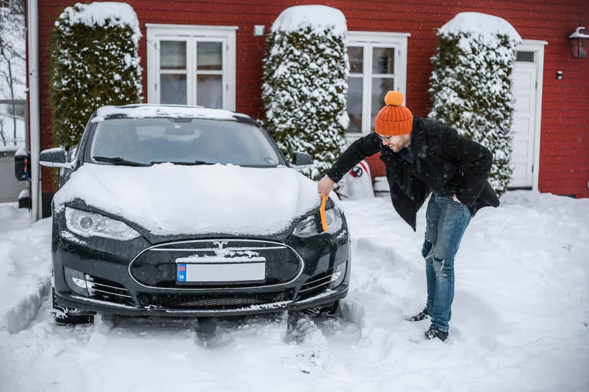 dark green Tesla model s is an electric car with Scandinavian cottage on the background