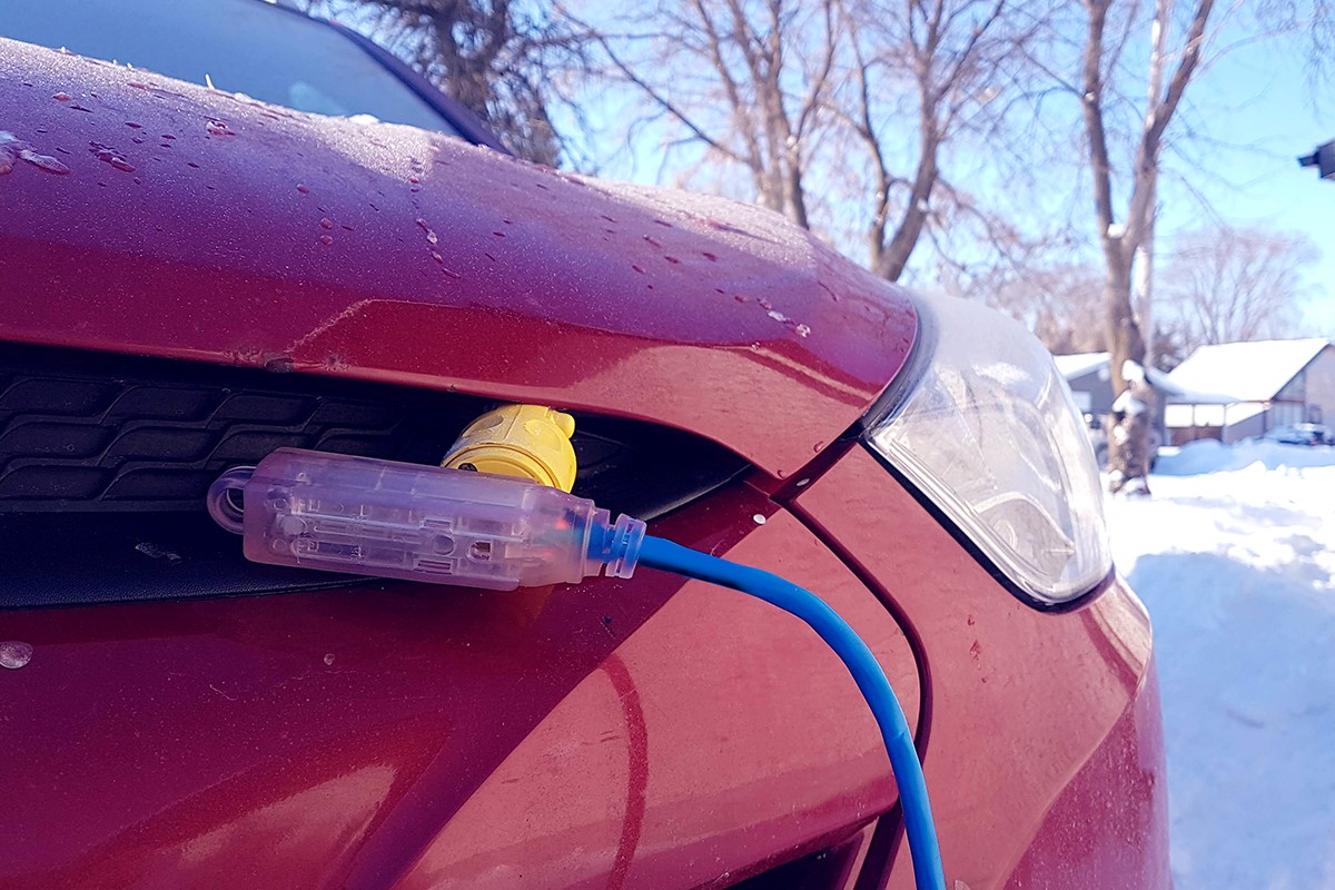 A block heater cable is plugged into a vehicle parked in a snowy winter driveway