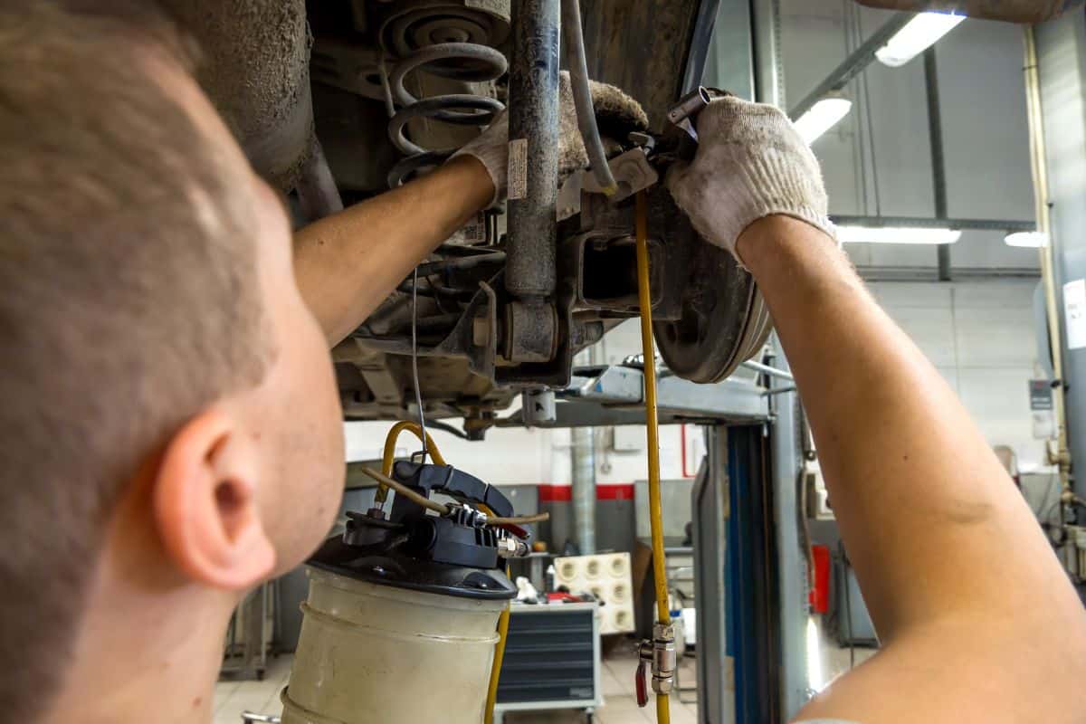 An auto mechanic connects a brake fluid replacement device to a brake drum fitting.